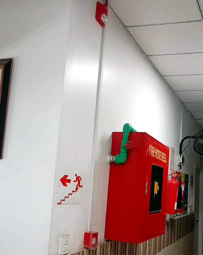Manual call point beside the fire hose reel, with a flasher sounder high on the corridor wall