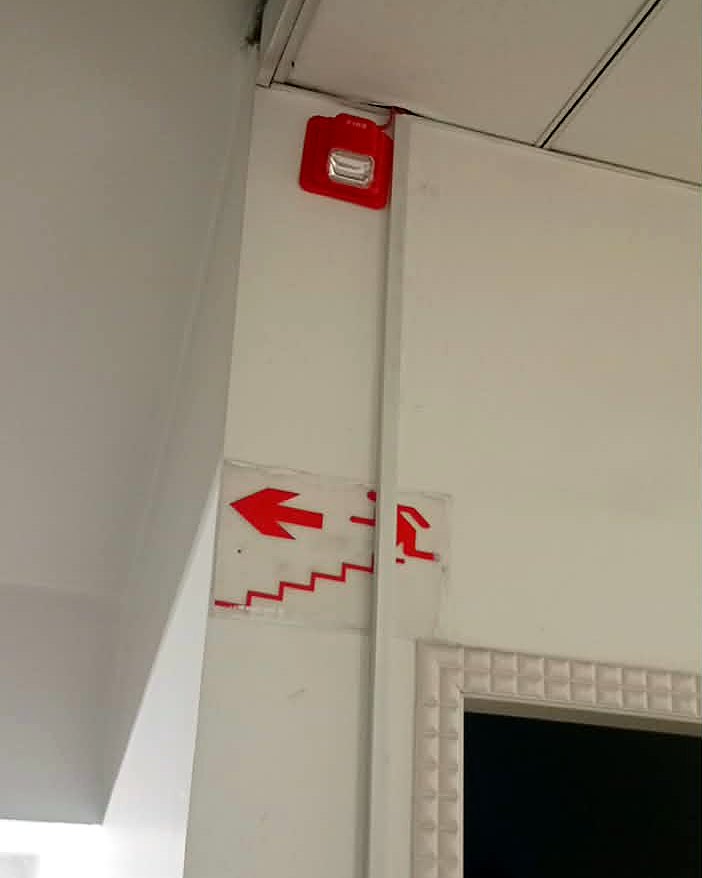 Flasher sounder mounted above the stairwell exit sign, visible down the escape route